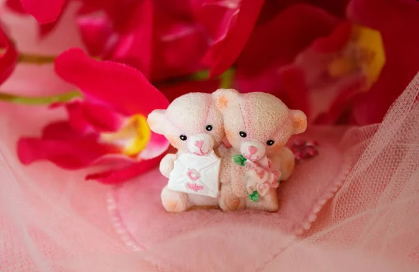 Sevgililer Günü için kalpleri ve çiçekleri olan pembe tekstil arka planında hatıra oyuncak ayılar.