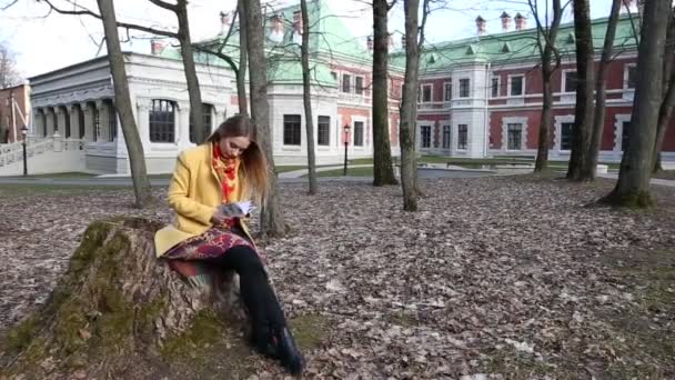 Молодая девушка сидит в старом парке замка и читает книгу в — стоковое видео