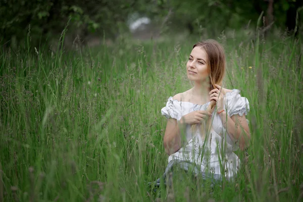 Chica rubia en pantalones cortos sentados en la hierba al aire libre — Foto de Stock