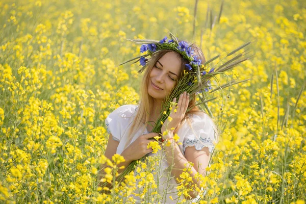 Menina com uma coroa de flores coloridas em sua cabeça, em um campo amarelo florido — Fotografia de Stock