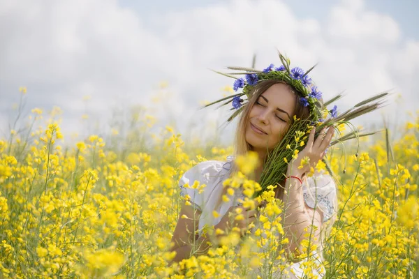 黄色開花フィールドで、彼女の頭の上のカラフルな花の花輪を持つ少女 — ストック写真