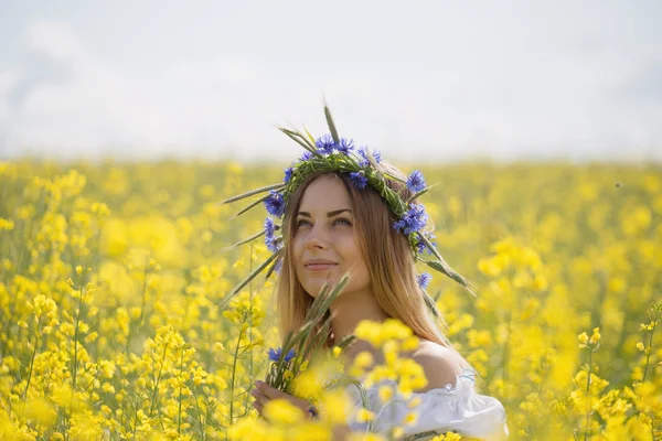 黄色開花フィールドで、彼女の頭の上のカラフルな花の花輪を持つ少女 — ストック写真