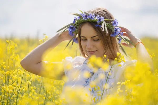 Fille avec une couronne de fleurs colorées sur la tête, dans un champ jaune fleuri — Photo