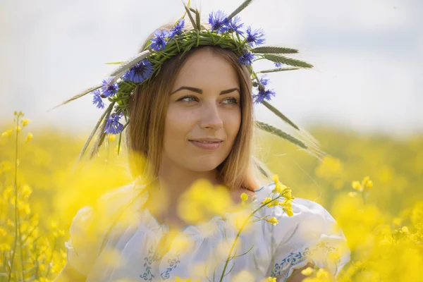 黄色開花フィールドで、彼女の頭の上のカラフルな花の花輪を持つ少女 — ストック写真