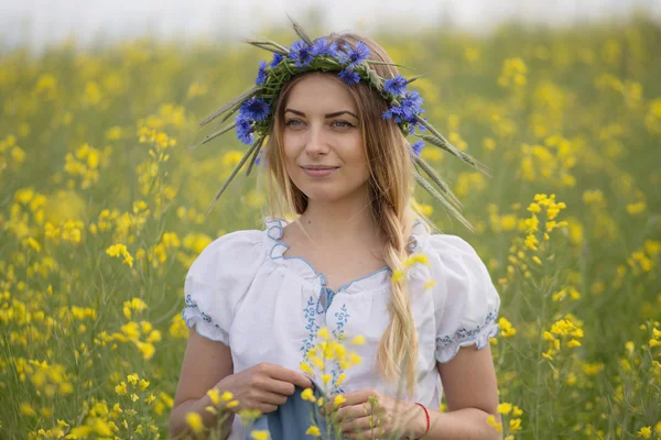 黄色開花フィールドで、彼女の頭の上のカラフルな花の花輪を持つ少女 — ストック写真