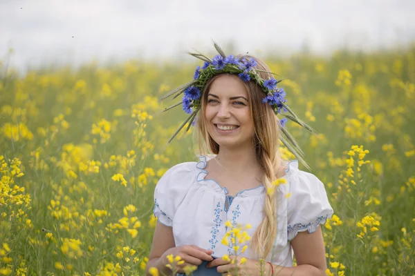 黄色開花フィールドで、彼女の頭の上のカラフルな花の花輪を持つ少女 — ストック写真