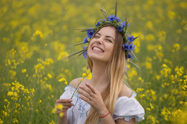 Menina com uma coroa de flores coloridas em sua cabeça, em um campo amarelo florido — Fotografia de Stock