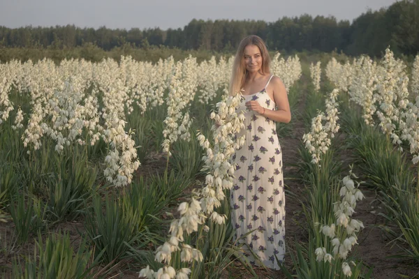 Prinzessin. junge hübsche Frau posiert in langem Abendkleid vor Büschen mit weißen Blumen — Stockfoto