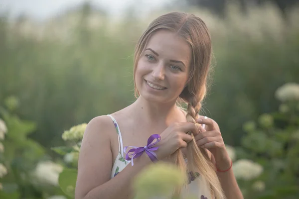 Unga vackra kvinnan i varma strålar från kvällssolen gå på ett grönt fält med vita blommor. — Stockfoto