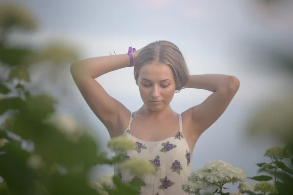 Jeune belle femme dans les rayons chauds du soleil du soir marchant sur un champ vert avec des fleurs blanches . — Photo