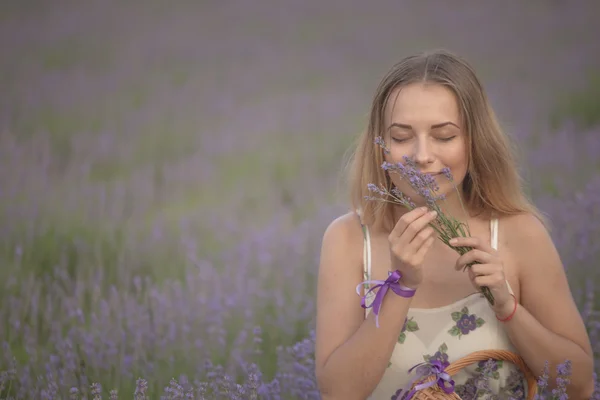 Menina sorridente cheirando flores em um campo de lavanda — Fotografia de Stock
