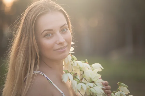 Szczegół portret... Młody piękny ładna kobieta stwarzających w długiej sukni przeciwko w polu z białych kwiatów — Zdjęcie stockowe