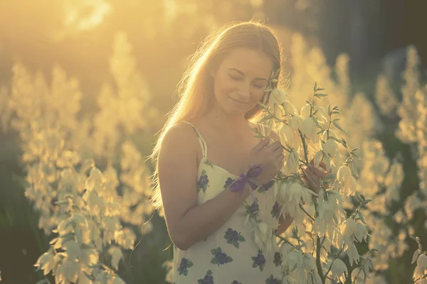 Princesa. Jovem bela mulher bonita posando em vestido longo contra no campo com flores brancas — Fotografia de Stock