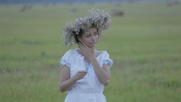 Joven chica en una corona de flores se encuentra solo en un campo abierto — Vídeos de Stock