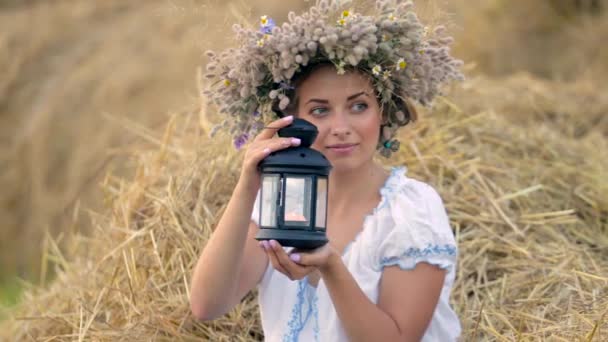Una giovane ragazza che indossa una corona che tiene una lanterna vicino alle pile di paglia . — Video Stock