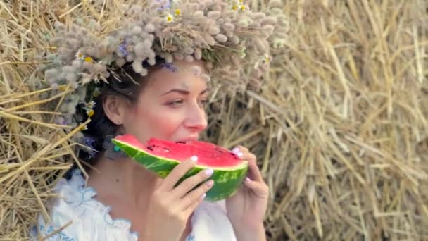 Junges Mädchen im Kranz isst reife Wassermelone in der Nähe der Strohstapel — Stockvideo