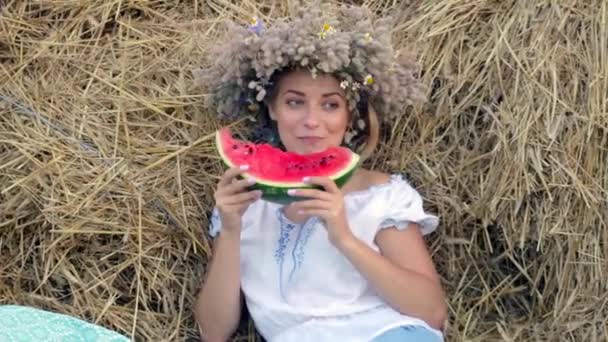 Jeune fille dans une couronne mange pastèque mûre près des piles de paille — Video