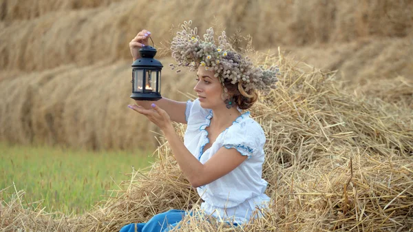 Uma jovem usando uma coroa segurando uma lanterna perto das pilhas de palha — Fotografia de Stock