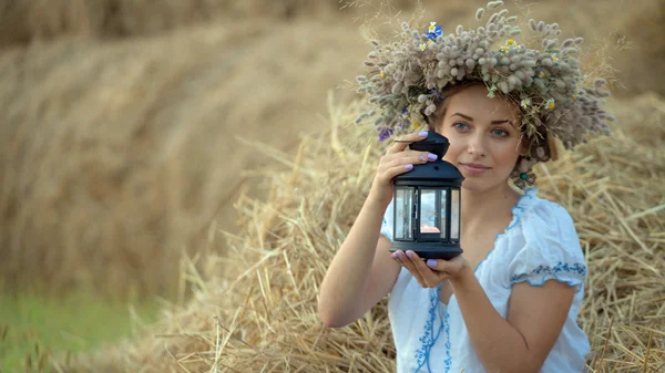 Uma jovem usando uma coroa segurando uma lanterna perto das pilhas de palha — Fotografia de Stock