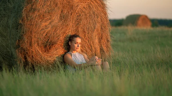 Menina bonita descansando em pilhas de feno ao pôr do sol — Fotografia de Stock