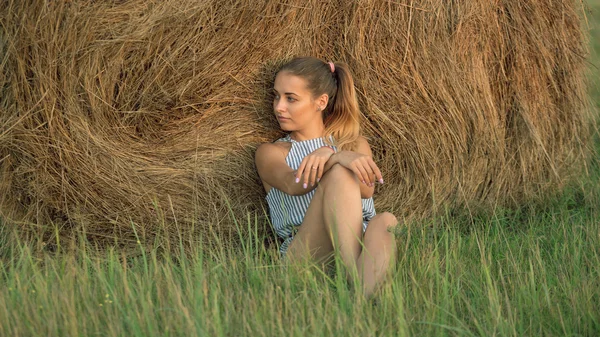 Menina bonita descansando em pilhas de feno ao pôr do sol — Fotografia de Stock