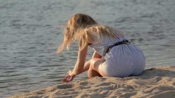 Дівчина відпочиває на піску біля річки ввечері — стокове відео