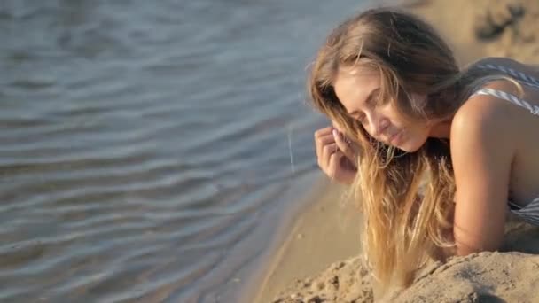 Dziewczyna odpoczynek na piasku w pobliżu rzeki wieczorem — Wideo stockowe