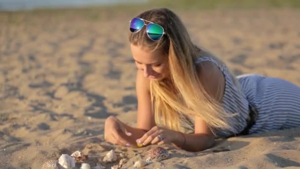 Девушка отдыхает на песке у реки вечером — стоковое видео