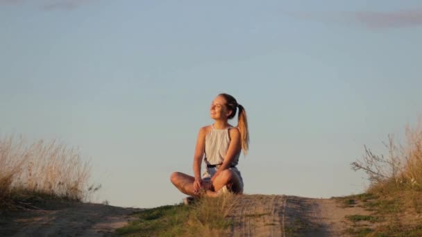 Beautiful young girl meditating on the hill in the rays of the setting sun — Stock Video