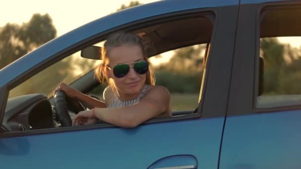 Hermosa joven sentada en el coche conduciendo hacia el atardecer . — Vídeo de stock