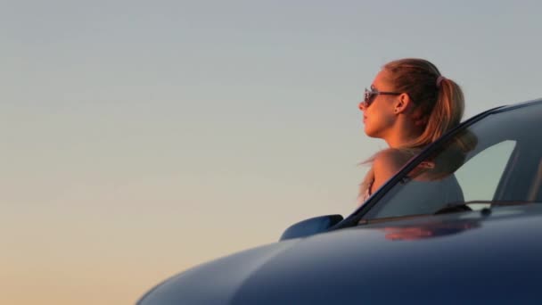 Mooi jong meisje permanent op de auto in de zonsondergang — Stockvideo