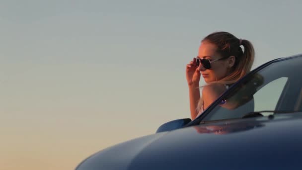 Hermosa joven de pie en el coche en la puesta del sol — Vídeo de stock