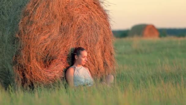 Krásná mladá dívka odpočívající na hromádky sena při západu slunce — Stock video