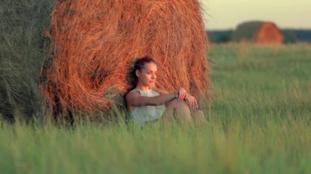 Hermosa joven descansando en pilas de heno al atardecer — Vídeos de Stock