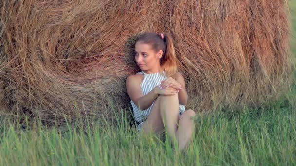 Красива молода дівчина відпочиває в стосах сіна на заході сонця — стокове відео