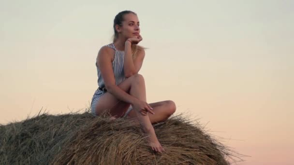 Beautiful young girl resting at stacks of hay at sunset — Stock Video