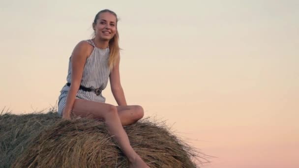 Beautiful young girl resting at stacks of hay at sunset — Stock Video