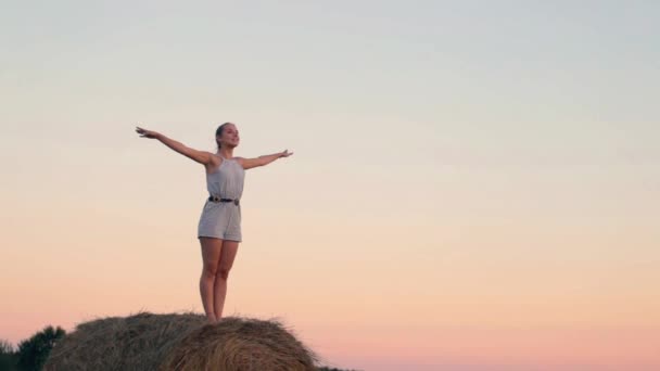 Beautiful young girl resting at stacks of hay at sunset — Stock Video