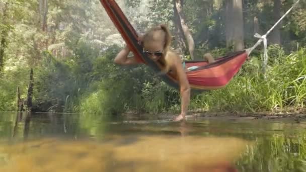 Красива дівчина катається на гамаку над водою . — стокове відео