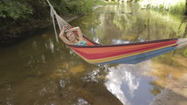 Девушка в купальнике, лежащая в гамаке над водой — стоковое видео