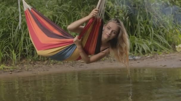 Hermosa chica montando en una hamaca sobre el río y el agua toca la mano — Vídeos de Stock