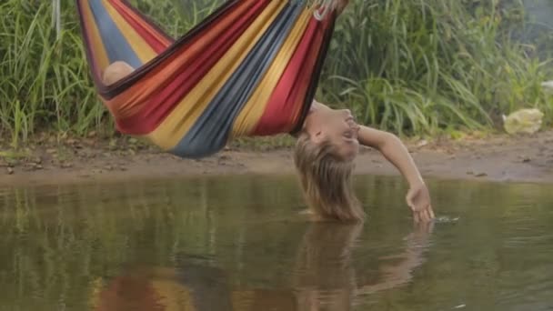 Mooi meisje rijden in een hangmat over de rivier en het water raakt de hand — Stockvideo