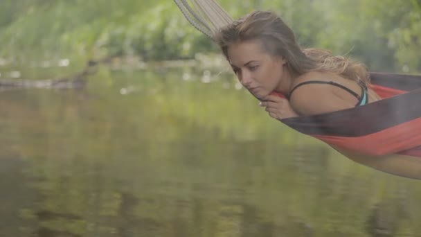 Gyönyörű lány lovaglás egy függőágyban a víz felett. — Stock videók