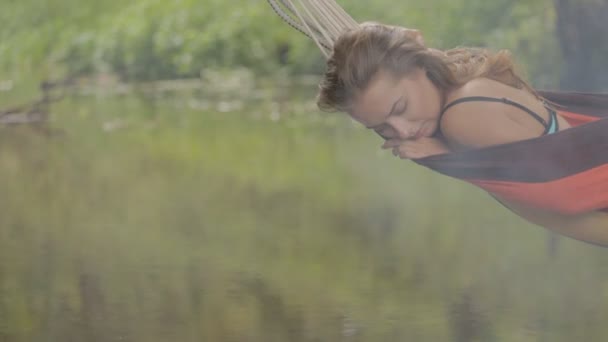 Vacker flicka ridning i en hängmatta över vattnet. — Stockvideo