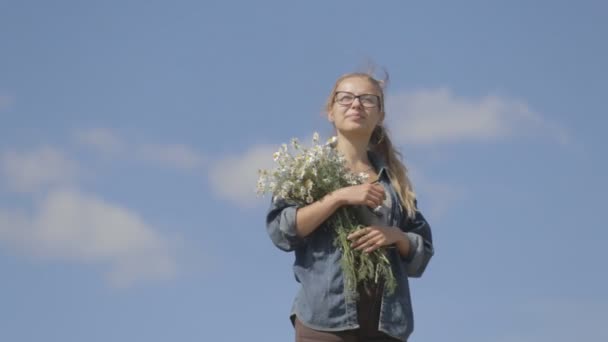 Chica con un ramo de margaritas sobre un fondo de cielo azul — Vídeos de Stock