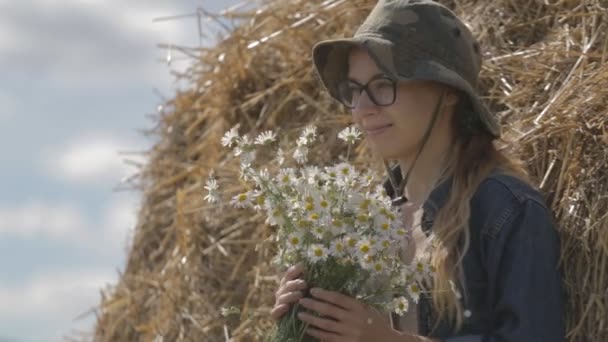 Mädchen mit Hut und Blumenstrauß steht an einem Stapel Stroh — Stockvideo