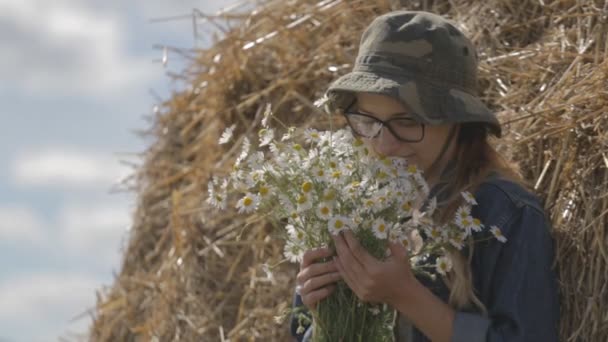 Дівчина в капелюсі з букетом квітів знаходиться в стосі соломи — стокове відео