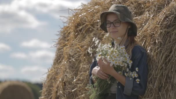 Chica en un sombrero con un ramo de flores está en la pila de paja — Vídeo de stock