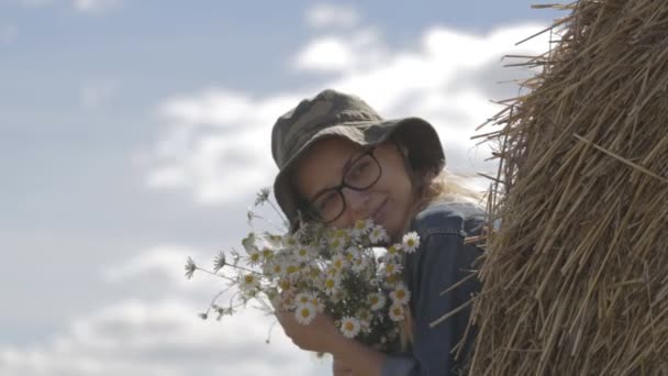 Дівчина в капелюсі з букетом квітів знаходиться в стосі соломи — стокове відео