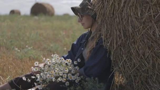 Chica en un sombrero con un ramo de flores sentado en la pila de paja — Vídeo de stock